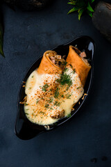 Baked thin pancakes with chicken, pineapple and onion with cheese sauce decorated with greens in a cast-iron bowl.