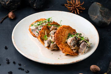 Draniki with beef and mushrooms in a creamy sauce in a plate.