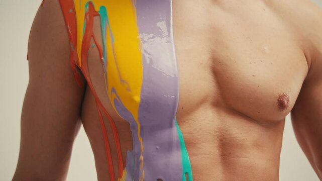 Colourful paint flowing over the man body close-up. Body art therapy with many various of paints. Painting on human body.