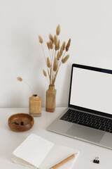 Open notebook with stationary, vases with dried flowers and laptop on the white desk. Back to school minimalistic modernt still life. Screen mock up for your text or image.