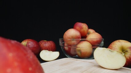Macrography of apples displayed in various forms: whole, sliced, and within a glass bowl with black background. Each close-up shot captures the red colors of the apples on cutting board. Comestible.