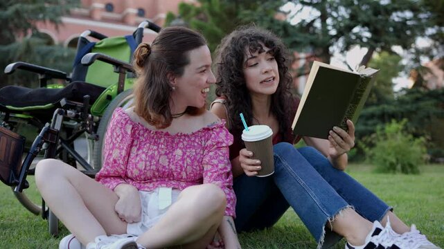 A caregiver shares a peaceful moment reading a book with a young woman with cerebral palsy, enjoying coffee on the grass in a park. Social caregiver reading with young woman with cerebral palsy in par