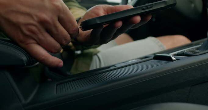 A man connects a mobile phone with a cable to a car while sitting in the driver's seat. Close-up of his hands, an unrecognizable person