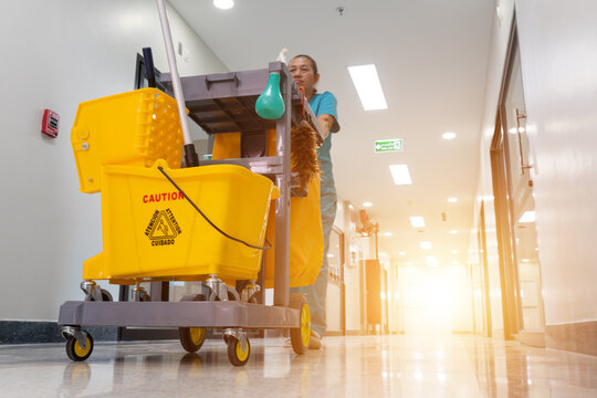 A woman is cleaning a hallway with a yellow bucket and a mop