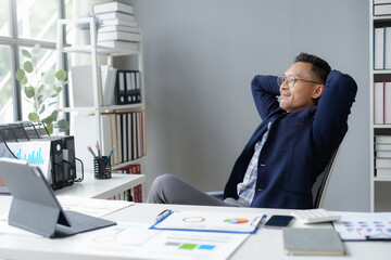 Asian businessman relaxing with his hands behind head sitting at his desk in a luminous office