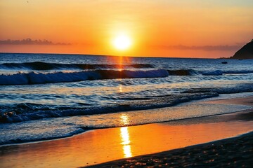 Naklejka premium A beautiful sunset over the ocean on a peaceful beach, perfect for relaxation and contemplation