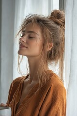 Fototapeta premium Young woman enjoying a quiet moment by the window with a mug in hand in soft morning light