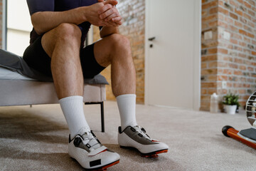 A man is sitting on the bed preparing for workout on the simulator, close-up of his legs, an...