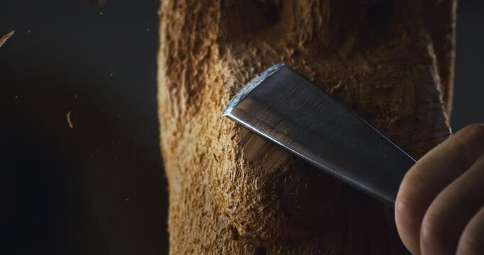 Super slow motion close up of artisan carpenter is working piece of wood with chisel for crafting wood artistic sculpting items in his workshop studio at 1000 fps.