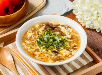 Hot and Sour Soup with Egg and Vegetables in bowl served on wooden tray napkin side view on table taiwan food
