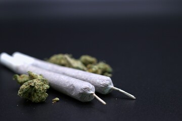 two rolled joints placed alongside scattered marijuana buds on a dark surface, banner with copy space. marijuana use and its effects, oblivion, drug legalization concept
