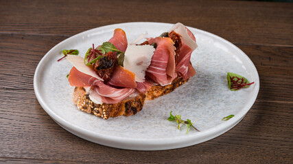 Bruschetta with bacon slices, capers, sun-dried tomatoes, parmesan cheese and greens.