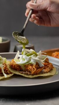 Vertical food video, mexican person serves some tinga tostadas with spicy green sauce