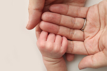 The newborn baby has a firm grip on the parent's finger after birth. Close-up little hand of child and palm of mother and father. Parenting, childcare and healthcare concept.