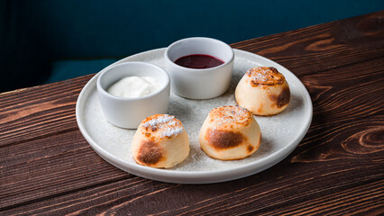 Cheese pancakes with berry sauce, sour cream and powdered sugar on a plate.