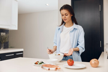 Woman preparing healthy meal in modern kitchen with bowl of food and plate of vegetables