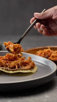 Vertical video, the hand of a dark skinned Mexican woman spreading chicken tinga on a tostada