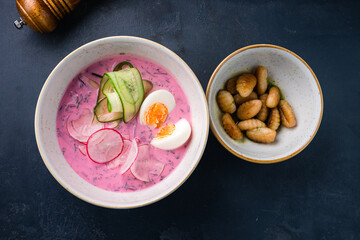 Beetroot soup with kefir, cucumber, egg and radish in bowl.