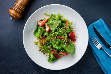 Green salad with strawberries, spinach, arugula, spices, sauce and sesame seeds.