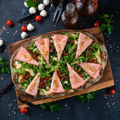 Italian cuisine pinza or pizza with ham, cheese, sun-dried tomatoes and arugula on rye dough.