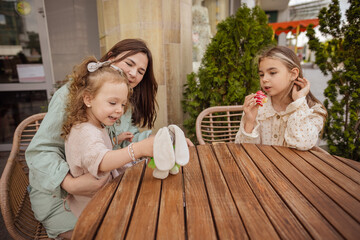 mom and daughters are sitting in a summer cafe and eating buns