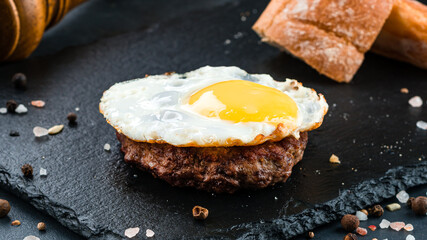 Fried fried eggs with beef cutlet, bread, salt and pepper on a dark background.