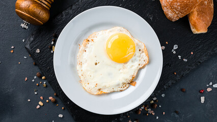 Fried eggs with bread, salt and pepper on a dark background.