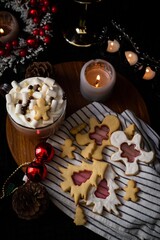 Cozy Christmas setting with hot chocolate full of marshmallows, gingerbread cookies, candles, baubles, and pine decorations.