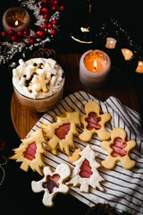 Cozy festive setting with hot cocoa, marshmallows, and homemade Christmas cookies on a dark wooden background, surrounded by holiday decorations.
