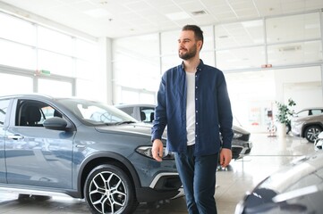 Handsome bearded buyer in casual wear in dealership, guy standing near car