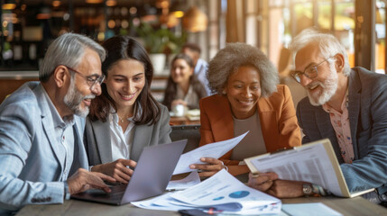 A group of four diverse professionals shares smiles while engaged in collaborative work around a table, sharing insights and laughter in a vibrant cafe atmosphere