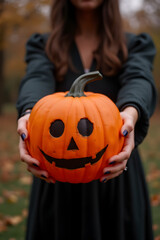 A woman dressed as a witch holds a carved pumpkin in a dimly lit street, showcasing her Halloween spirit. Ideal for Halloween-themed promotions, invites, or ads.
