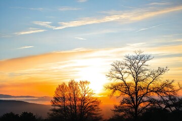 Fototapeta premium A serene landscape of the sun setting behind mountains and trees, with a warm glow