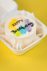Birthday cake in a white gift box on the yellow background. Little Korean bento cake with happy birthday text. Flat lay