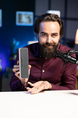 Cheerful online star doing technology review of Bluetooth portable speaker for online platforms channel. Joyful influencer showcasing music playing device to his viewership