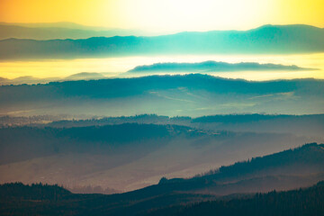 Layered mountain ridges under soft morning light with misty valleys and a golden sky in the distance