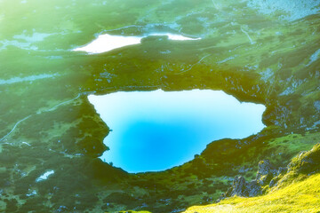 High-altitude mountain lake with crystal clear blue water surrounded by green slopes and rocky...