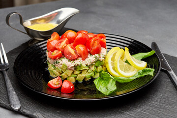 Fresh avocado and tuna salad topped with cherry tomatoes, garnished with lemon slices and basil