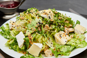 Fresh green salad with chicken, brie cheese, and sesame seeds, served with berry sauce on the side