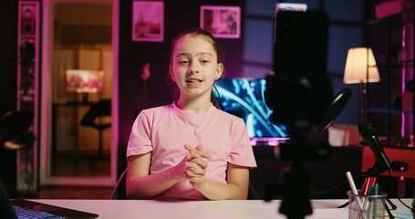 Close up shot on smartphone attached to tripod in living room used as professional studio for recording vlogs. Focus on phone camera capturing footage of kid in blurry background discussing topics