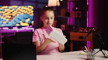 Kid content creator being sponsored by partnering brand to do unboxing video on her online channel. Little girl does influencer marketing, presenting social media followers product endorsement