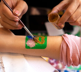 Kid's animator is creating a Shimmering sparkling glitter tattoo on a child's hand at a birthday party. Body art. High quality photo