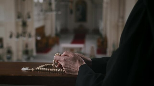 Cropped shot of hands of unrecognizable religious servant holding rosary while praying to Lord in Catholic Church