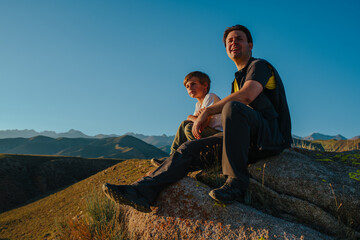 Father and son sitting on huge stone in the mountains at sunset light