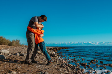 Happy father and son hugs standing on lake shore on summer day