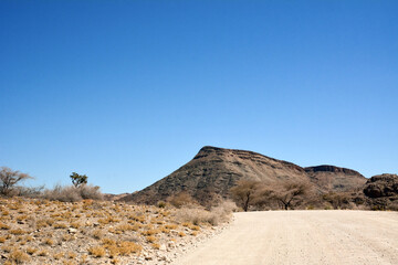 A dirt road in the desert in perspective leading to the hills under a clear blue sky