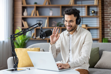 Smiling young man with headphones recording podcast from home office with laptop and microphone setup on desk