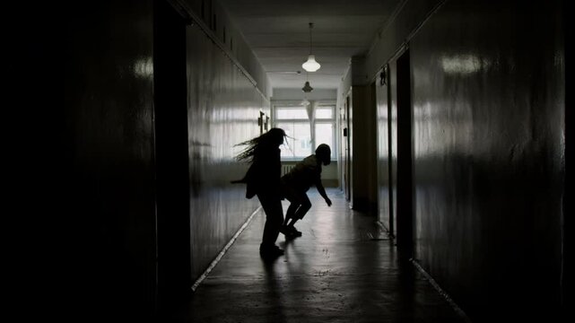 Silhouettes of male and female partners performing contemporary dance improvisation in dark hallway