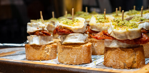 Typical snack of Basque Country, pinchos or pinxtos skewers with small pieces of bread, sundried tomatoes, goat cheese served in bar in San-Sebastian or Bilbao, Spain, close up