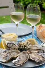 Plate with fresh live oysters with citron, bread, butter and white wine served at restaurant in oyster-farming village, Arcachon bay, Gujan-Mestras port, France